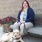 Shirek sitting outside on bench with Golden Retriever on ground in front of her. 